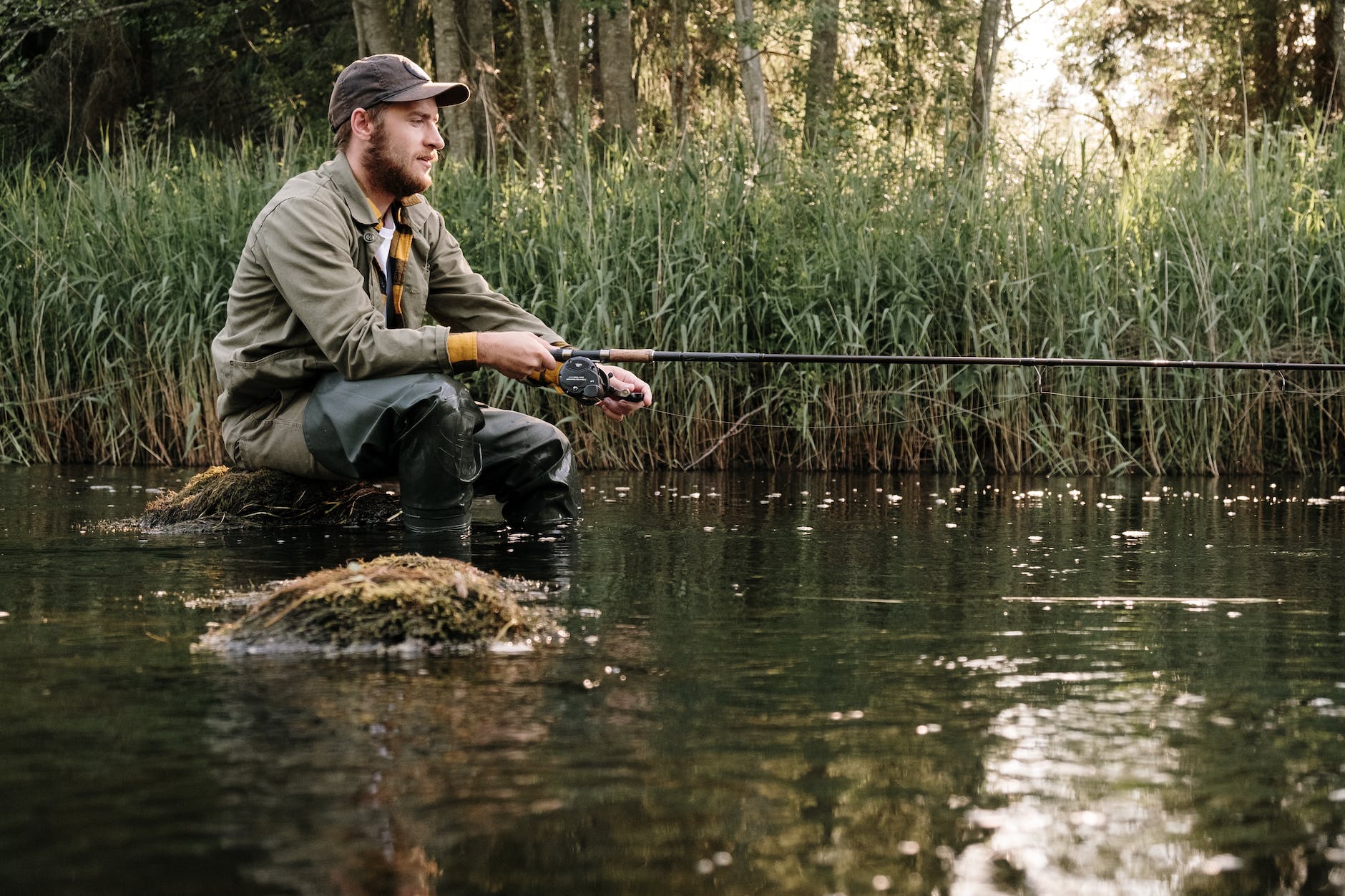 man in gray jacket and black pants sitting on brown rock in the river fishing with bobbers